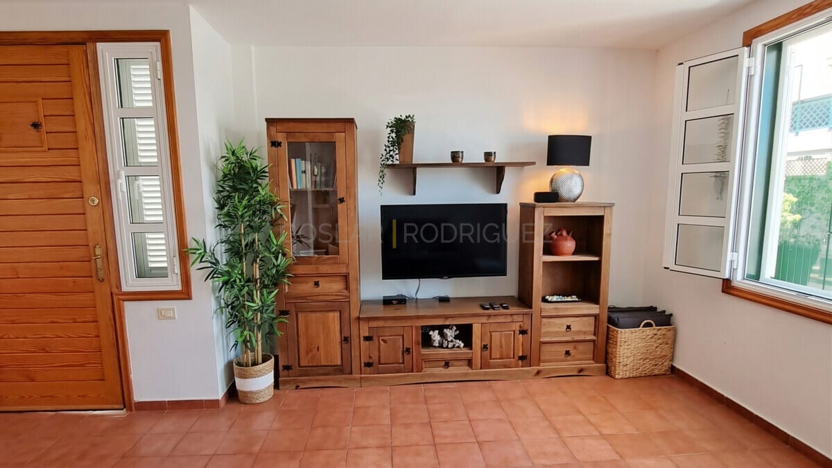 Gemütliches Wohnzimmer mit Holzmöbeln, TV, Pflanze und Terrakotta-Böden.