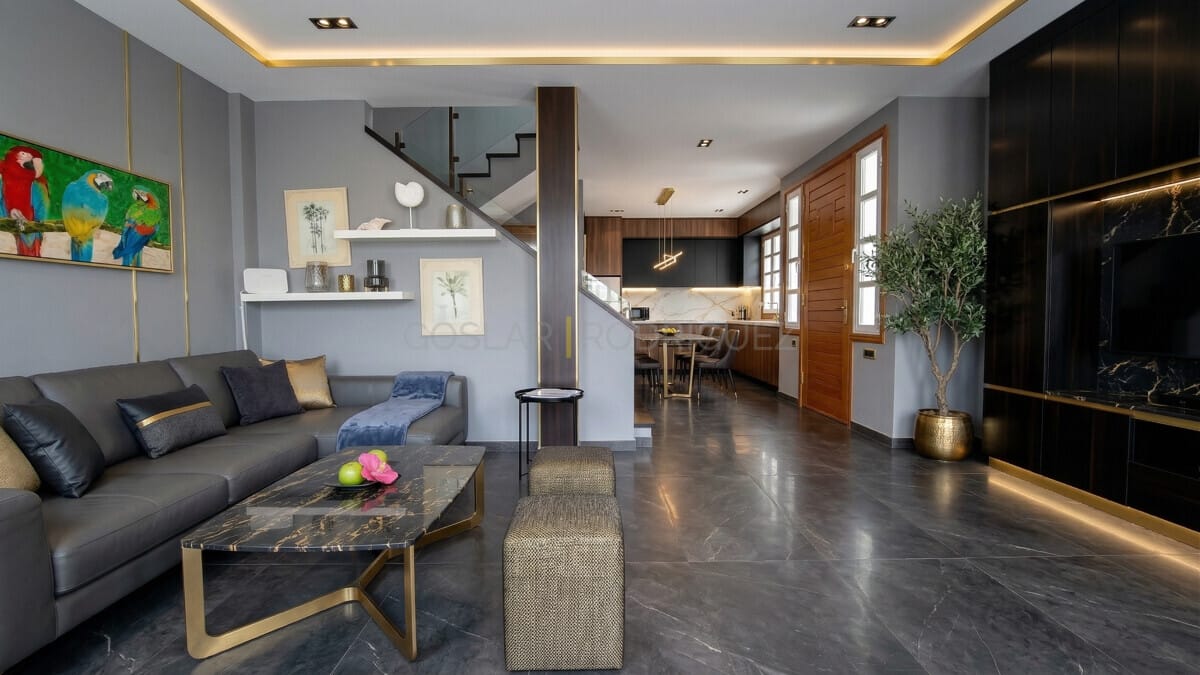 Modernes Luxus-Wohnzimmer mit grauem Sofa, Marmortisch und offener Küche. Goldene Akzente.