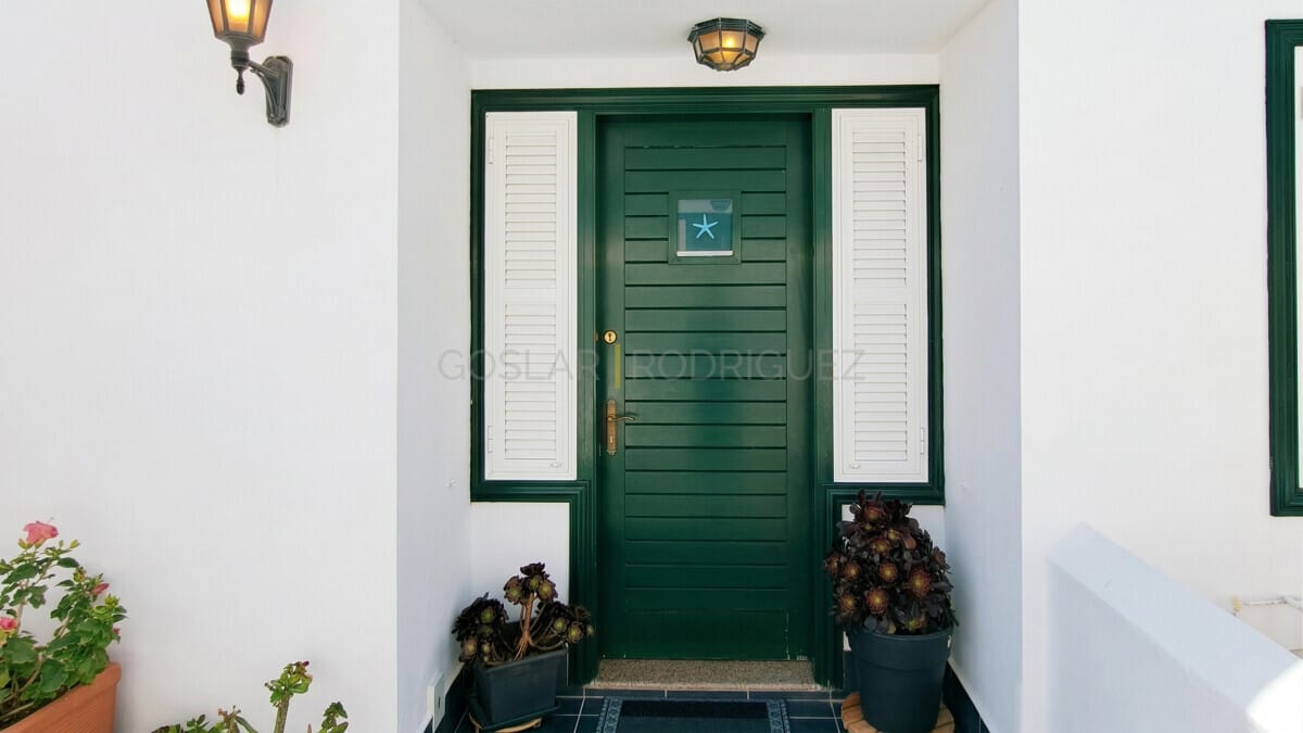 Elegante dunkelgrüne Haustür mit Seestern-Detail, flankiert von weißen Fensterläden und Topfpflanzen.