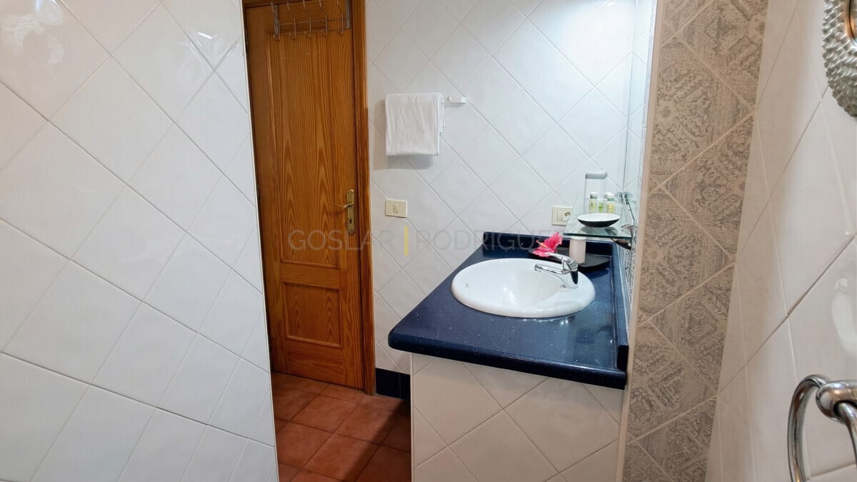 Modernes Badezimmer mit weißen Fliesen, blauem Waschtisch und Holztür.