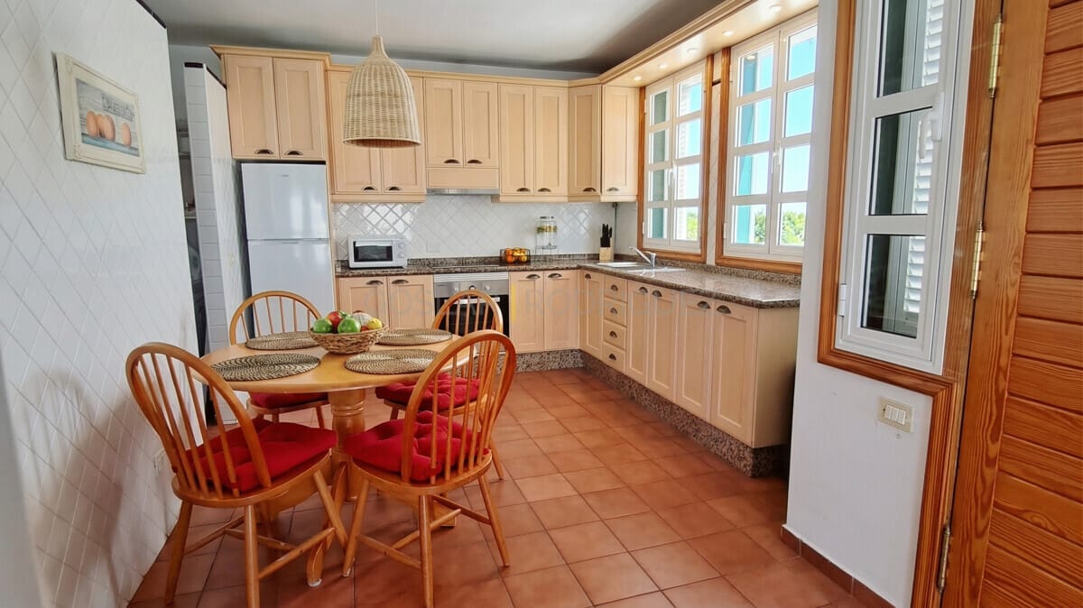 Helle Küche mit hellen Holzschränken, Esstisch und großen Fenstern.