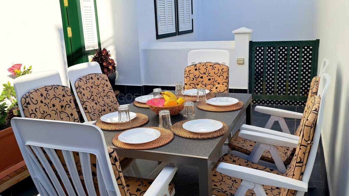 Gartensitzgruppe mit gemusterten Kissen auf gefliester Terrasse, ideal für Mahlzeiten im Freien.