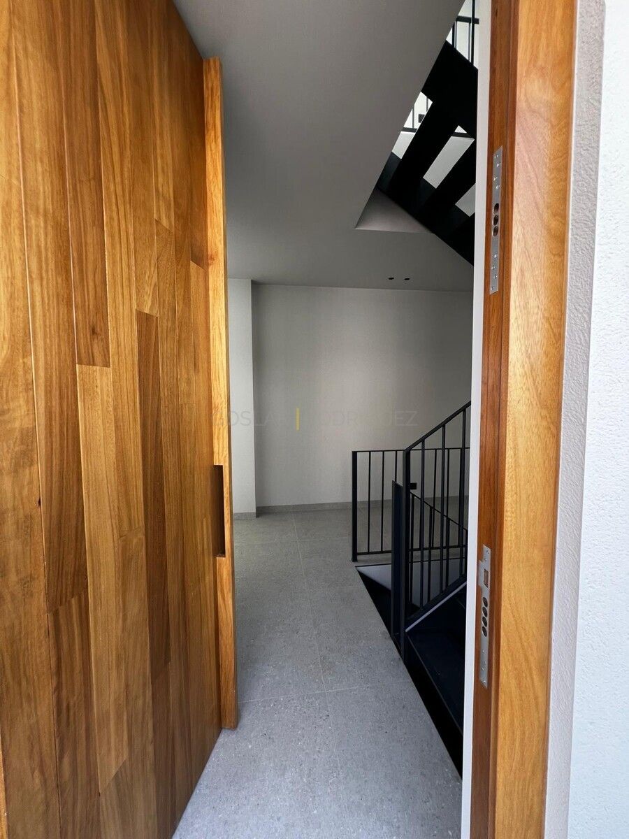 Eingangsbereich einer modernen Villa in Adeje auf Teneriffa. Blick durch eine offene Holztür auf das Treppenhaus mit schwarzem Geländer.