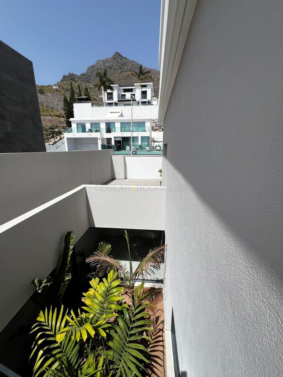 Aussenansicht einer modernen Villa in Adeje auf Teneriffa. Gepflegter Innenhof mit tropischen Pflanzen und im Hintergrund ein Gebäude mit Pool und Bergpanorama.