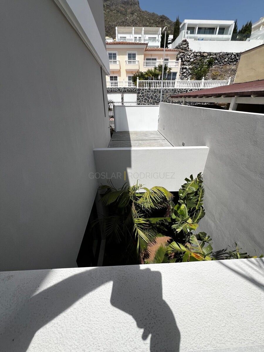 Blick von oben auf einen begrünten Innenhof einer Villa in Adeje auf Teneriffa. Die Pflanzen sind üppig und der Hof ist von hellen Mauern umgeben.