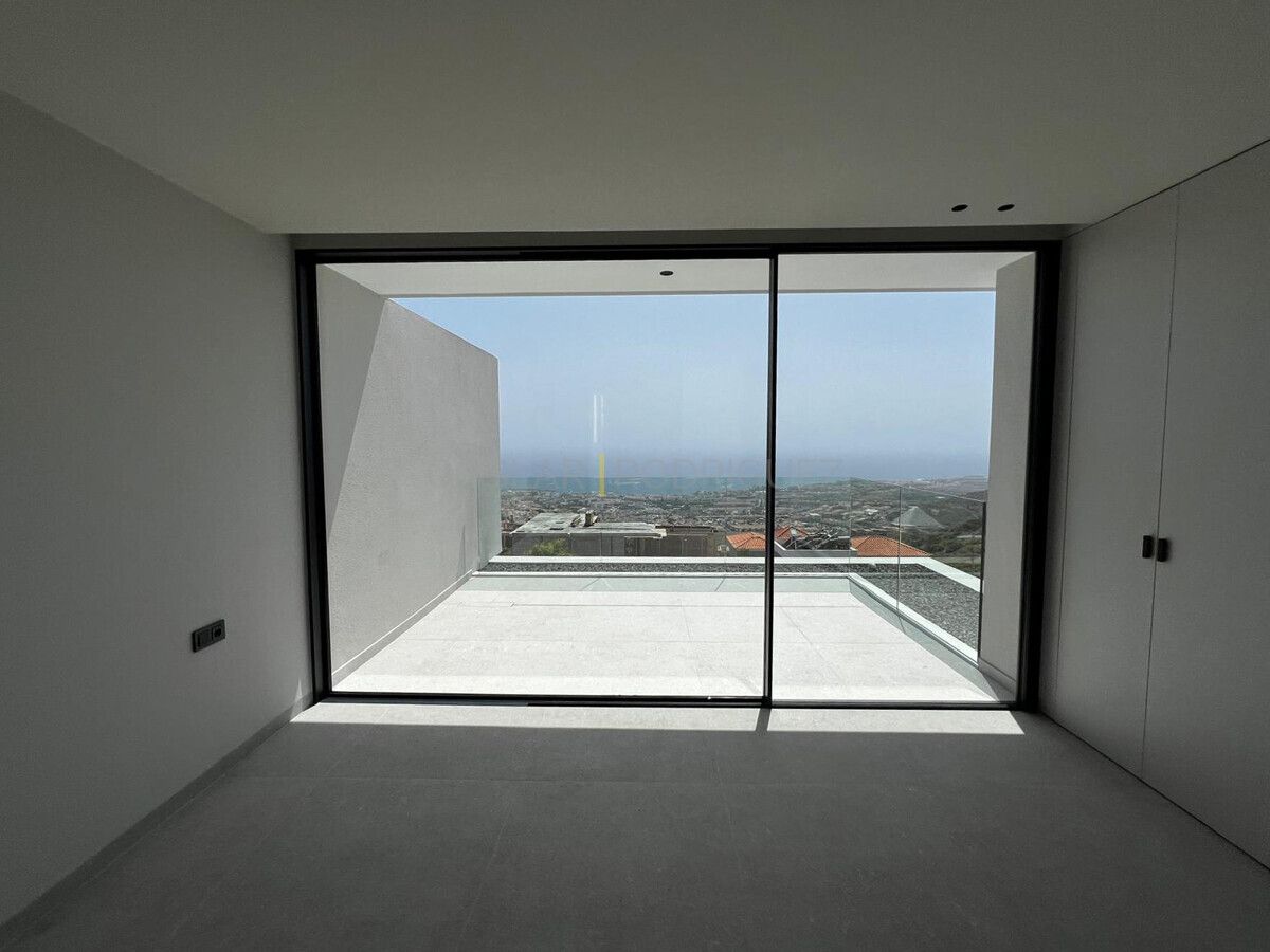 Heller Raum mit Schiebetür und Meerblick in einer Villa in Adeje, Teneriffa. Die Tür führt auf einen Balkon mit Glasgeländer und Blick auf die Küstenlinie und das Meer.