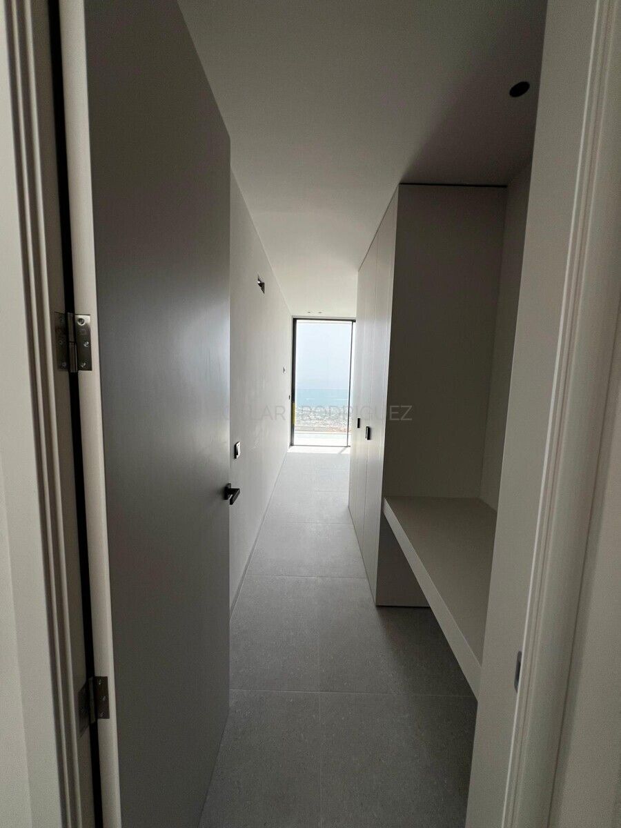 Innenansicht eines modernen Flurs mit Meerblick in einer Villa in Adeje, Teneriffa. Graue Fliesen und weiße Wände mit Einbauschränken führen zu einem Fenster mit Blick auf das Meer.