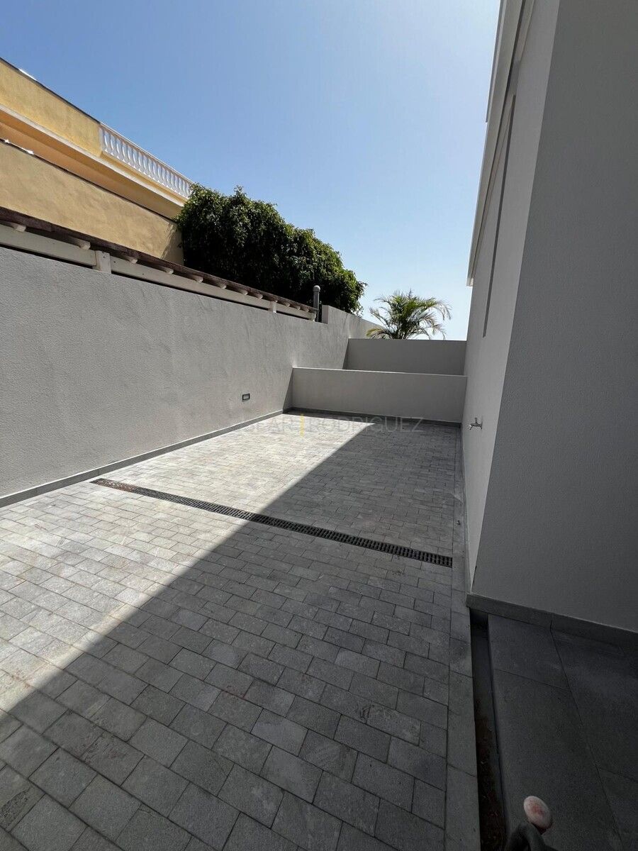 Aussenansicht eines gepflasterten Hofs in einer Villa in Adeje im Süden von Teneriffa. Blick auf Mauern, eine Palme und einen blauen Himmel.