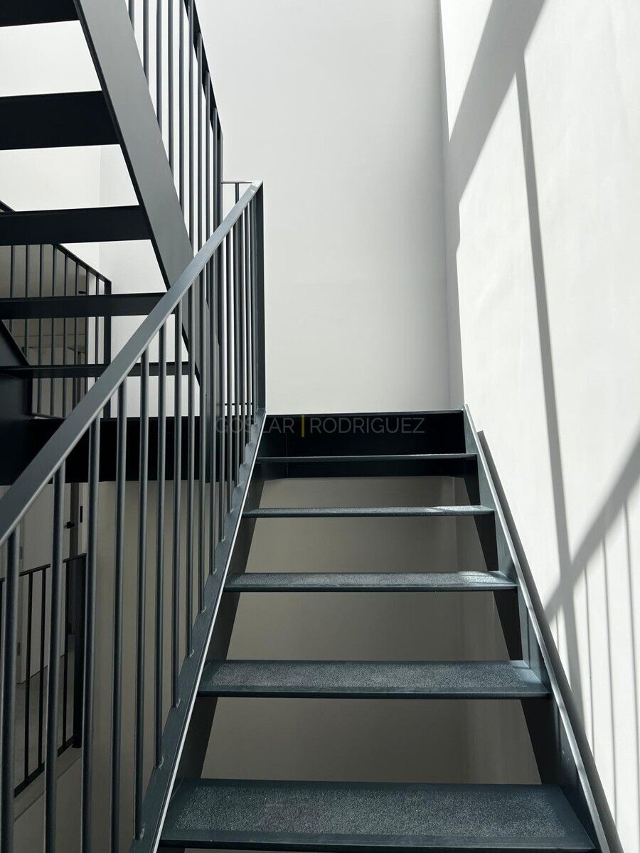 Detailaufnahme einer modernen Treppe in einer Villa in Adeje auf Teneriffa. Die Treppe ist aus dunklem Metall gefertigt und führt nach oben, während Sonnenlicht auf die weiße Wand fällt.