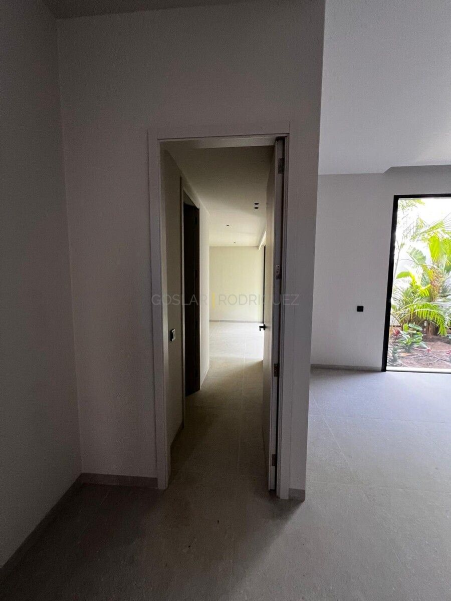 Innenaufnahme einer Villa in Adeje, Teneriffa. Blick durch eine offene Tür auf einen hellen Flur mit Fenster und Gartenblick.