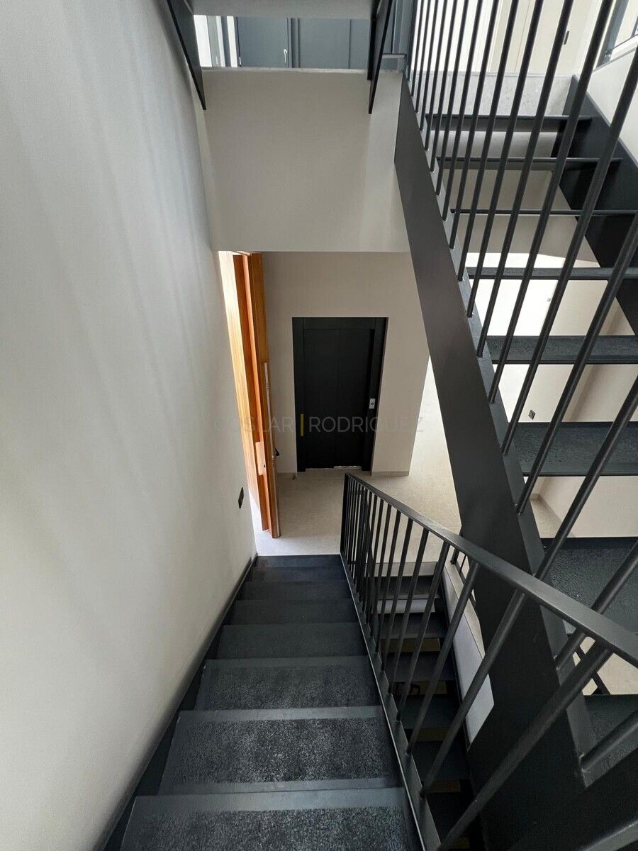 Innenaufnahme eines modernen Treppenhauses in einer Villa in Adeje auf Teneriffa. Die Treppe hat schwarze Stufen und ein Geländer aus Metall. Eine Holztür steht offen.