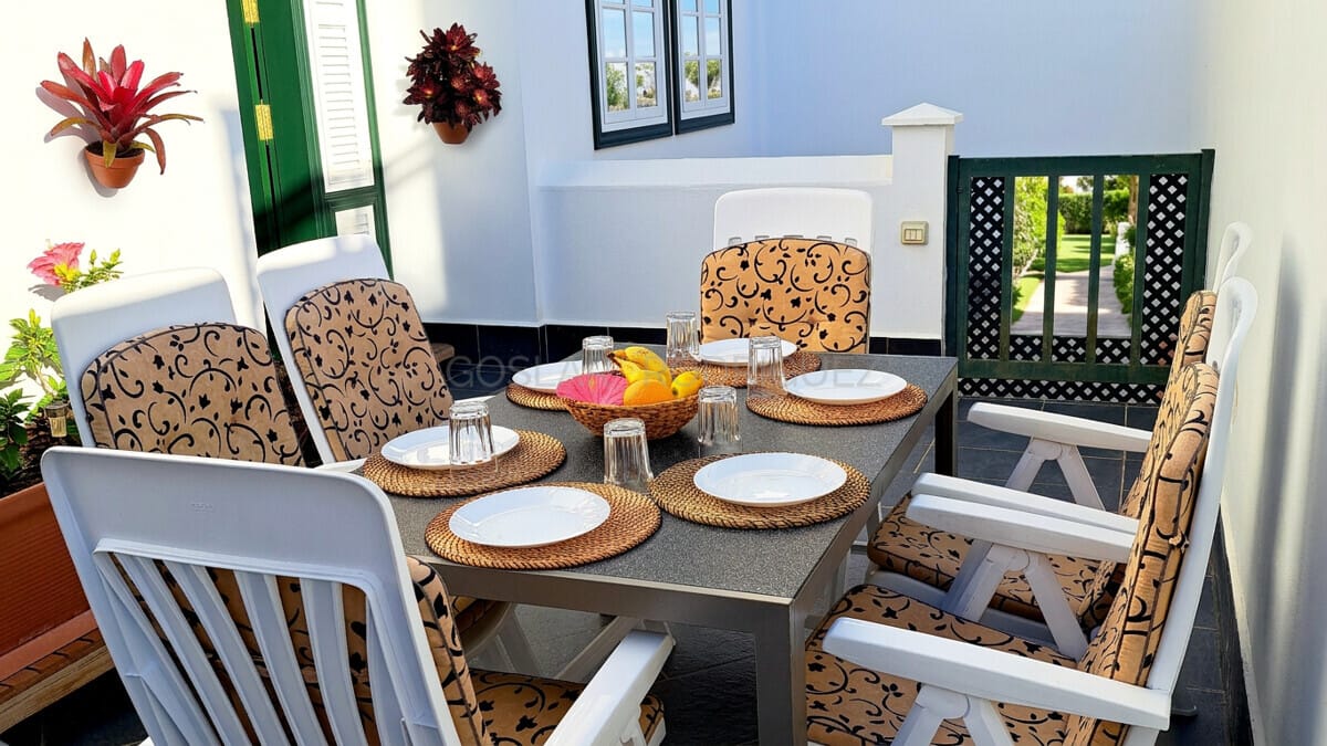 Terrace dining area with table set for six, surrounded by plants.