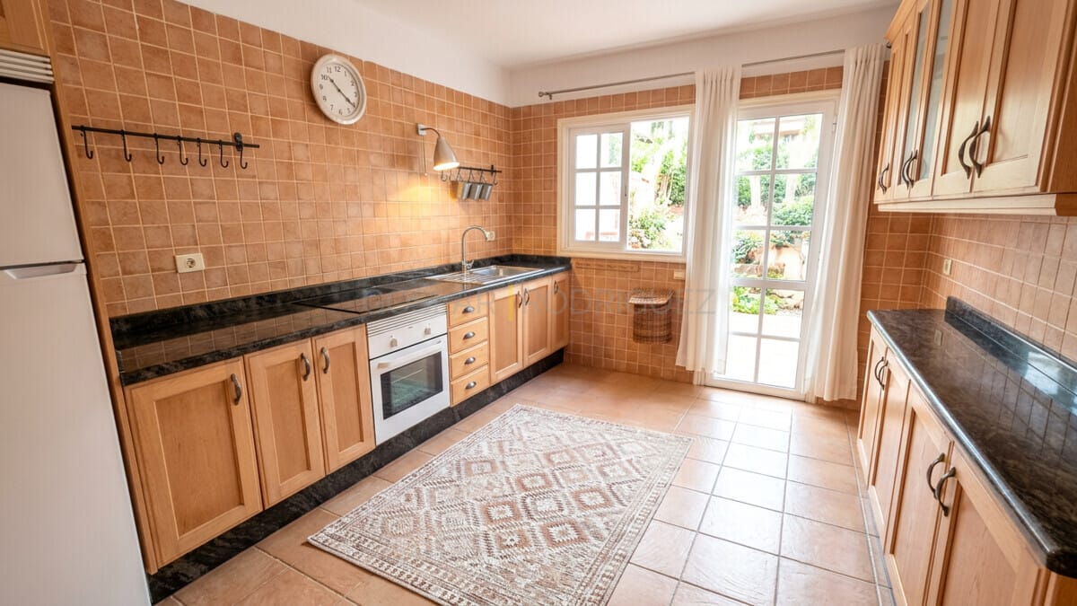Tiled kitchen with wooden cabinets and oven, overlooking a garden in Abades, Tenerife.