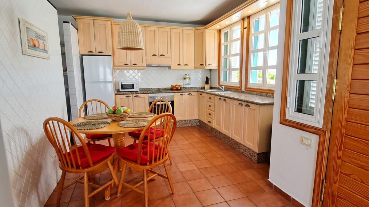 Bright kitchen with wooden cabinets, dining table, and natural light in Tenerife.