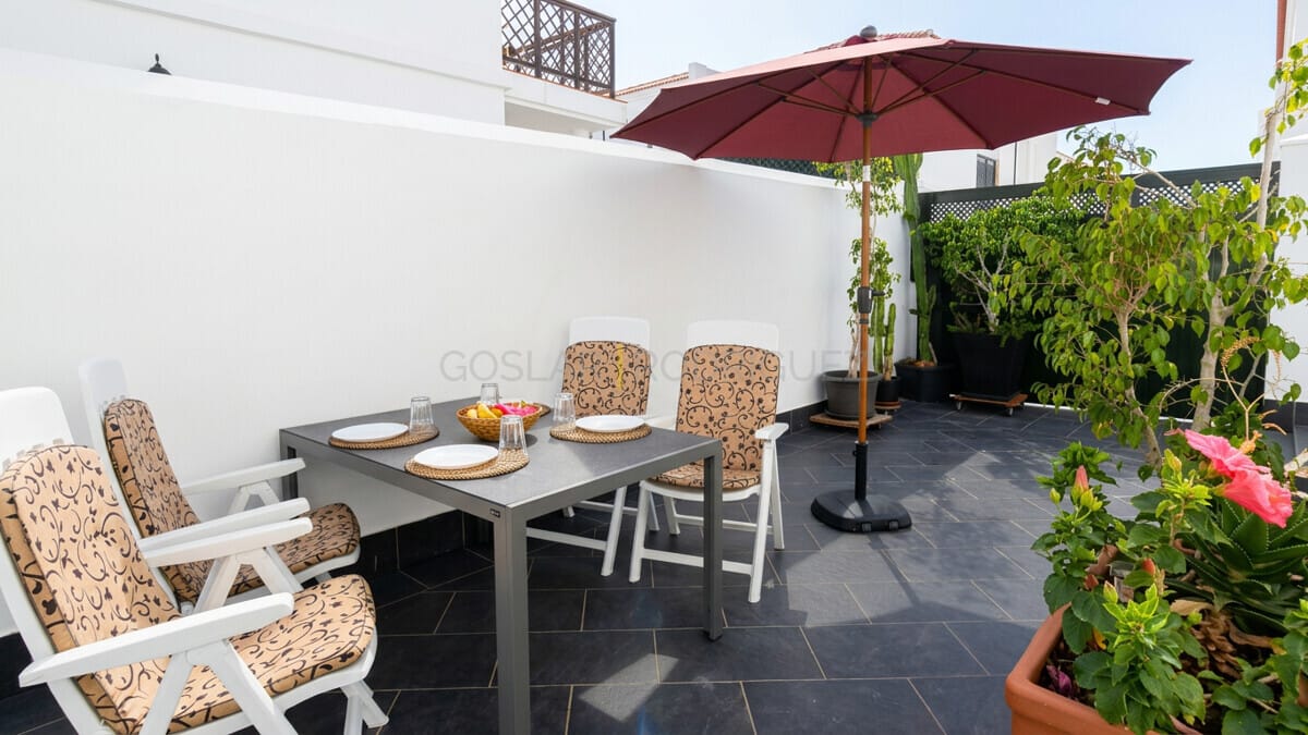 Sunny terrace with dining set and umbrella, green plants.